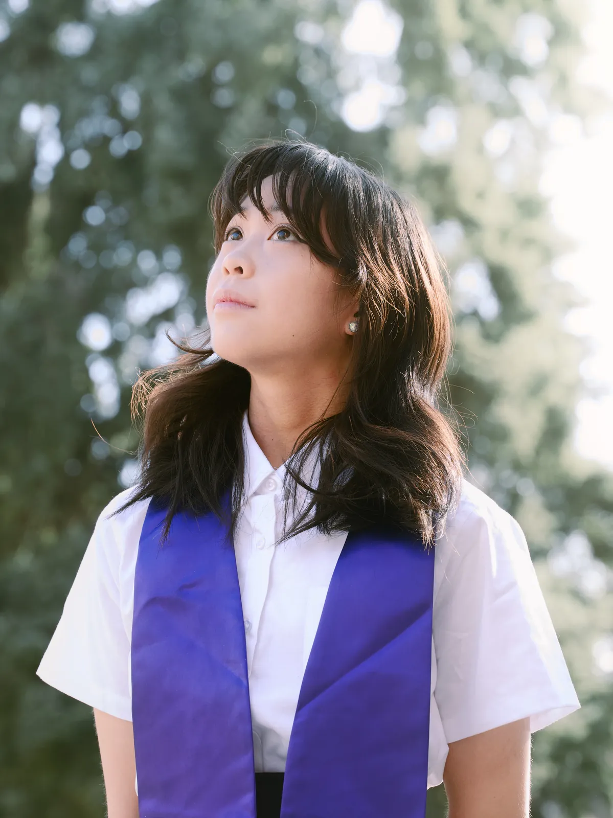 UW Graduate looking up thoughtfully under spring campus cherry blossoms