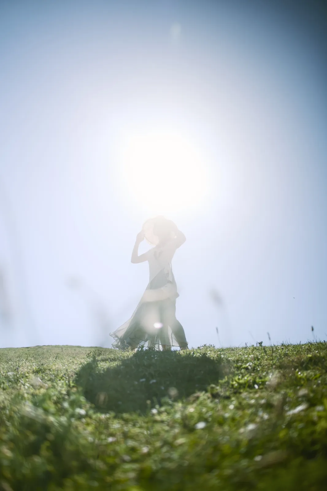 Scenic silhouette of a woman on a grassy hill backlit by brilliant sun, composition