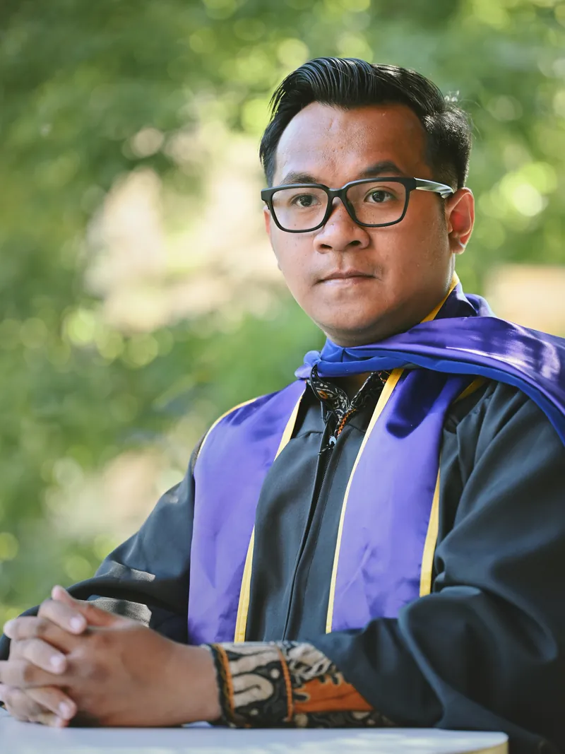 UW Foster School of Business master's graduate in cap gown and purple stole among campus ivy