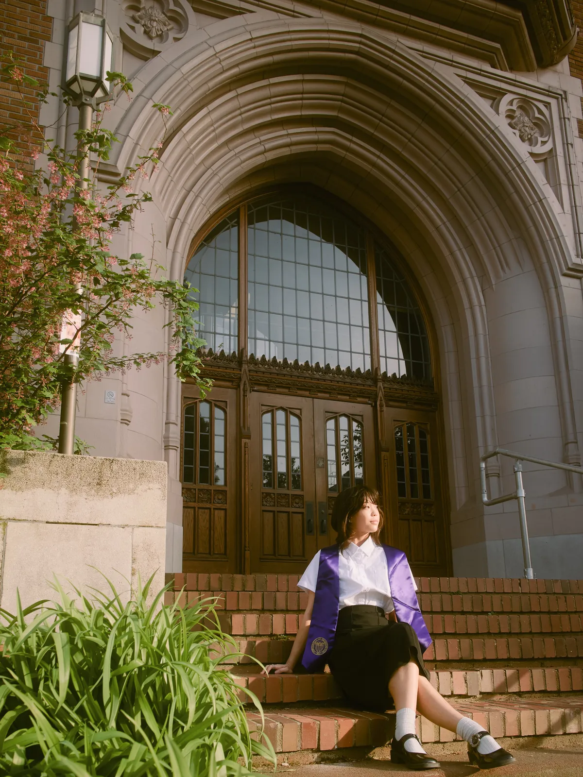 UW Senior sitting proudly on historic campus steps in graduation sash