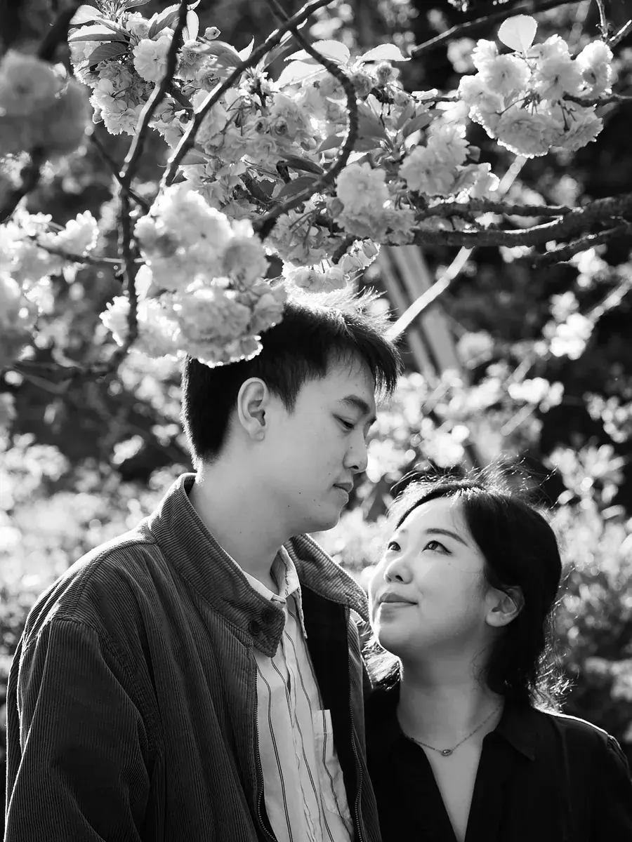 Intimate black-and-white close-up of a couple beneath tree blossoms