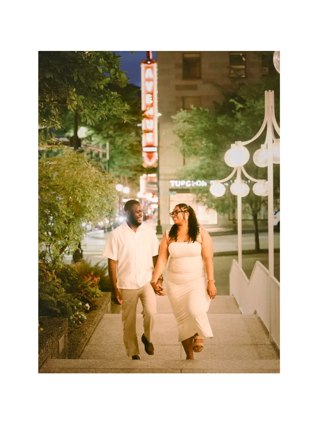 Engaged couple walking together beneath illuminated city signs