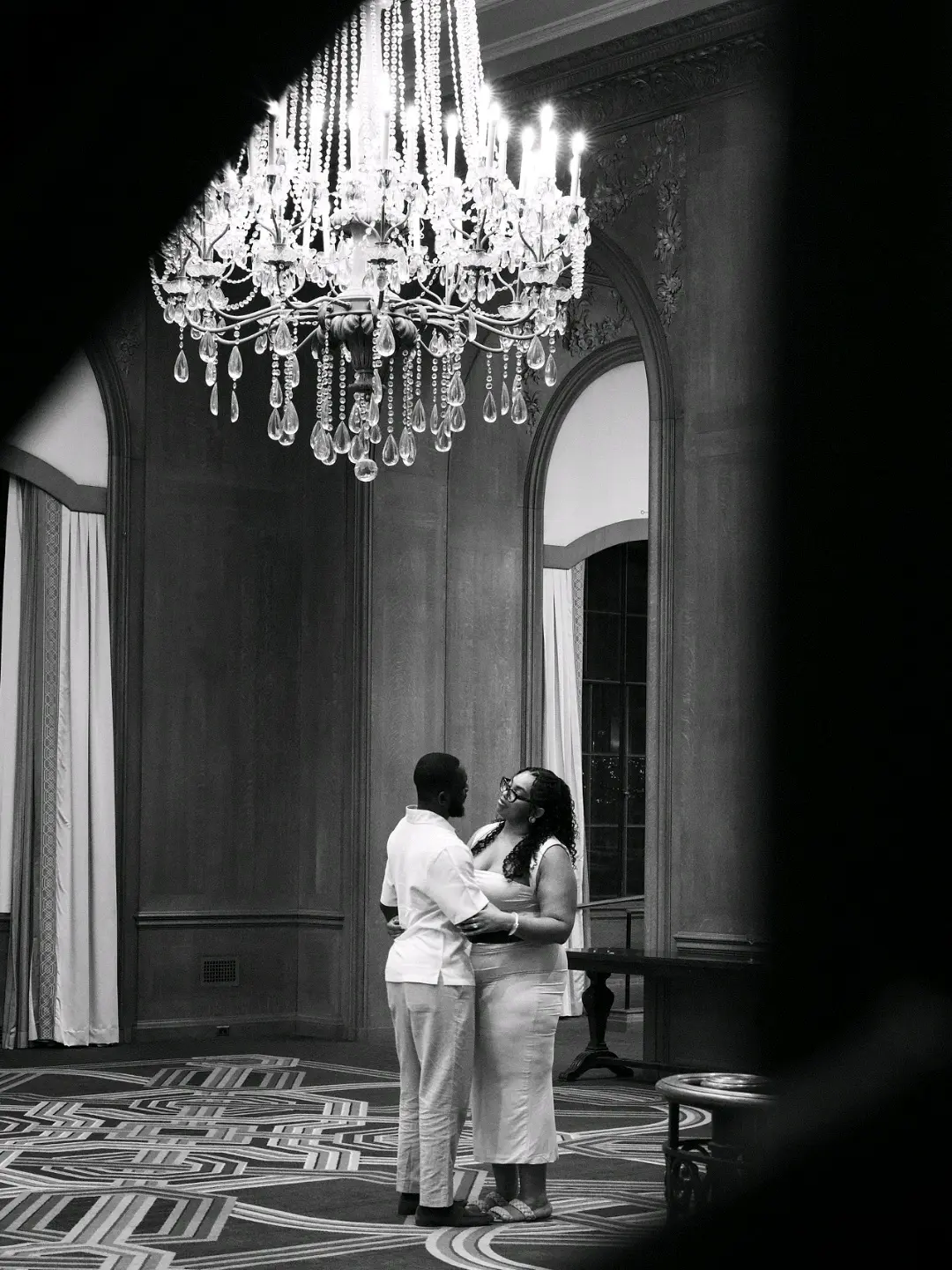 Black-and-white proposal beneath a chandelier in an ornate ballroom