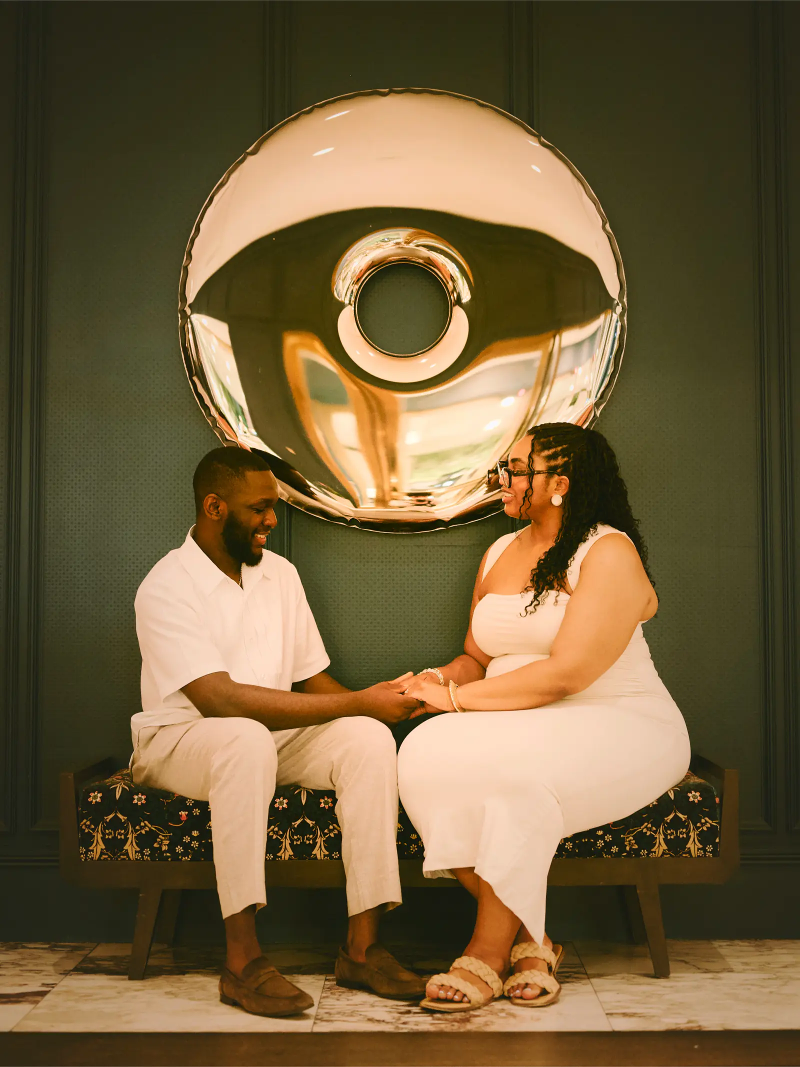Engaged couple seated beneath a circular mirrored sculpture