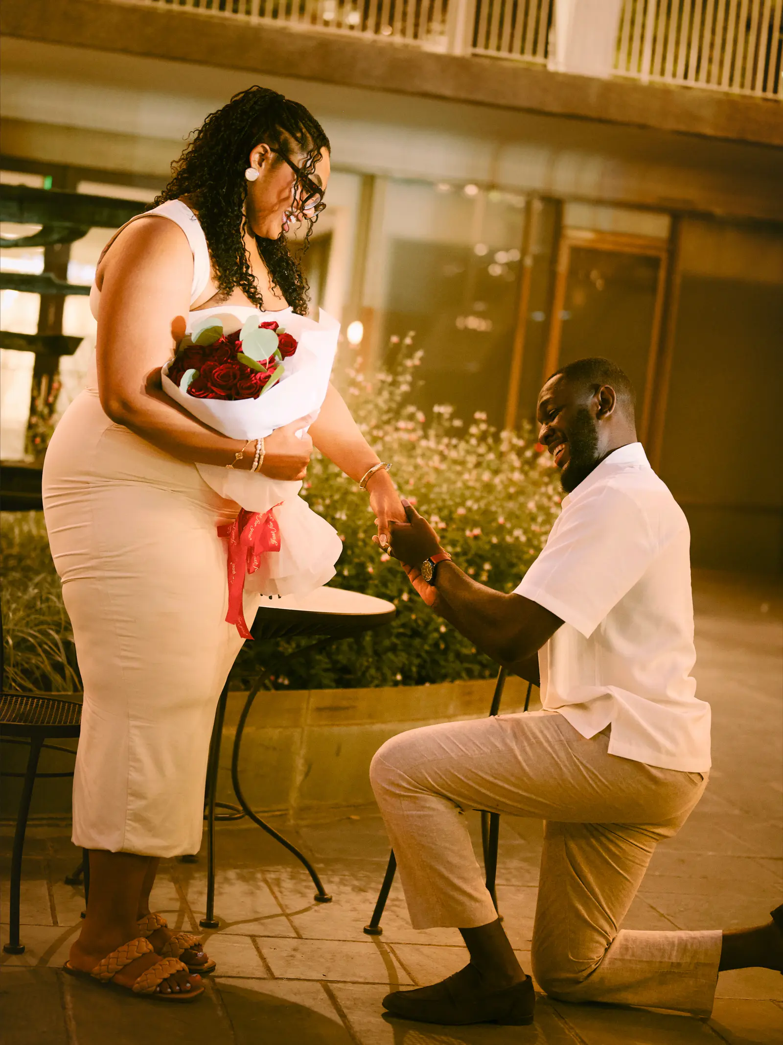 A partner kneels to propose on a city sidewalk at night
