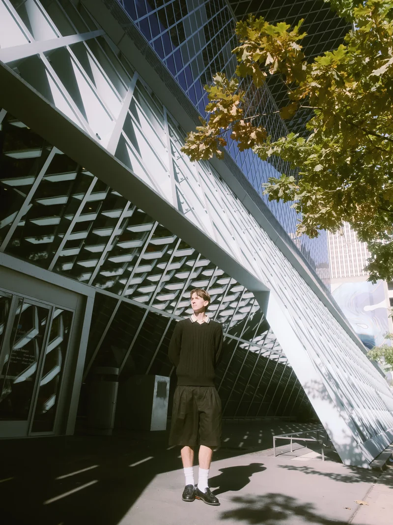 Senior under autumn oak leaves beside Seattle Central Library glass architecture