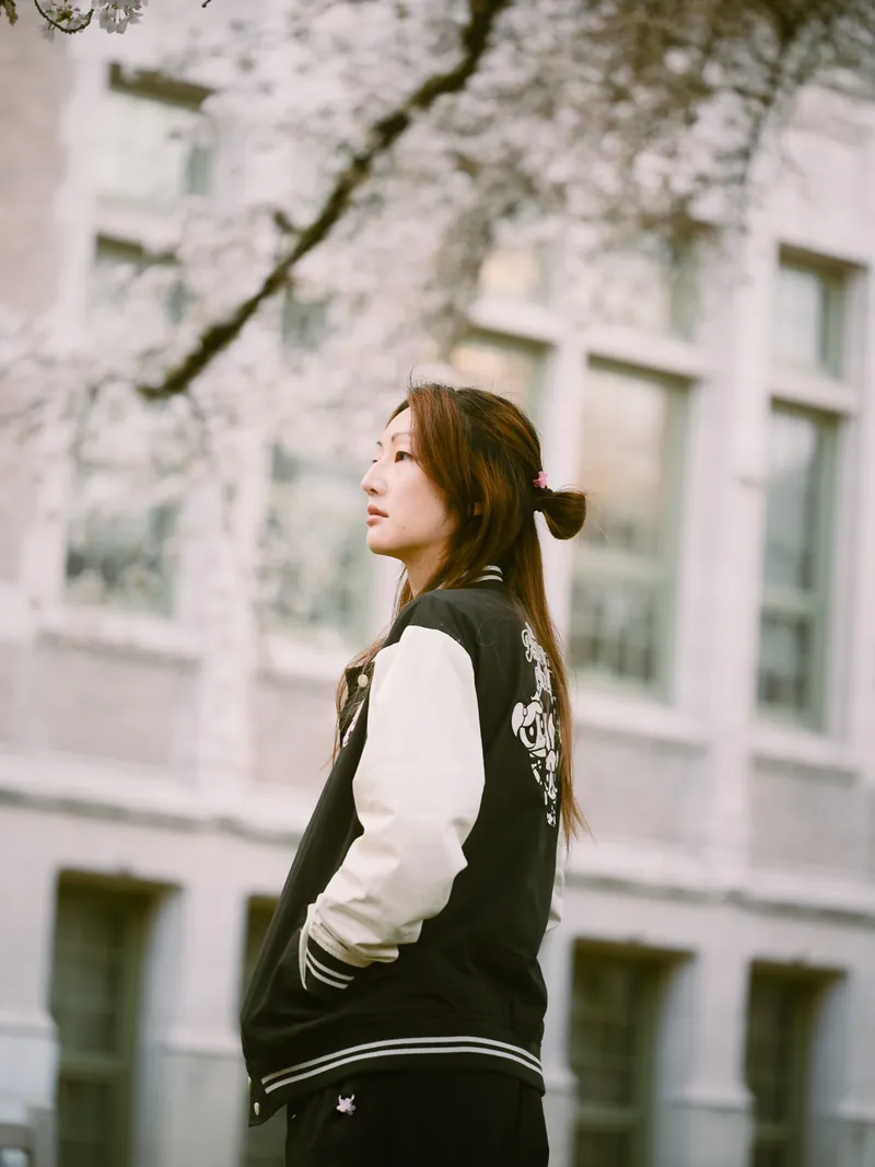 Seattle high school senior portrait in varsity bomber jacket with spring campus blooms