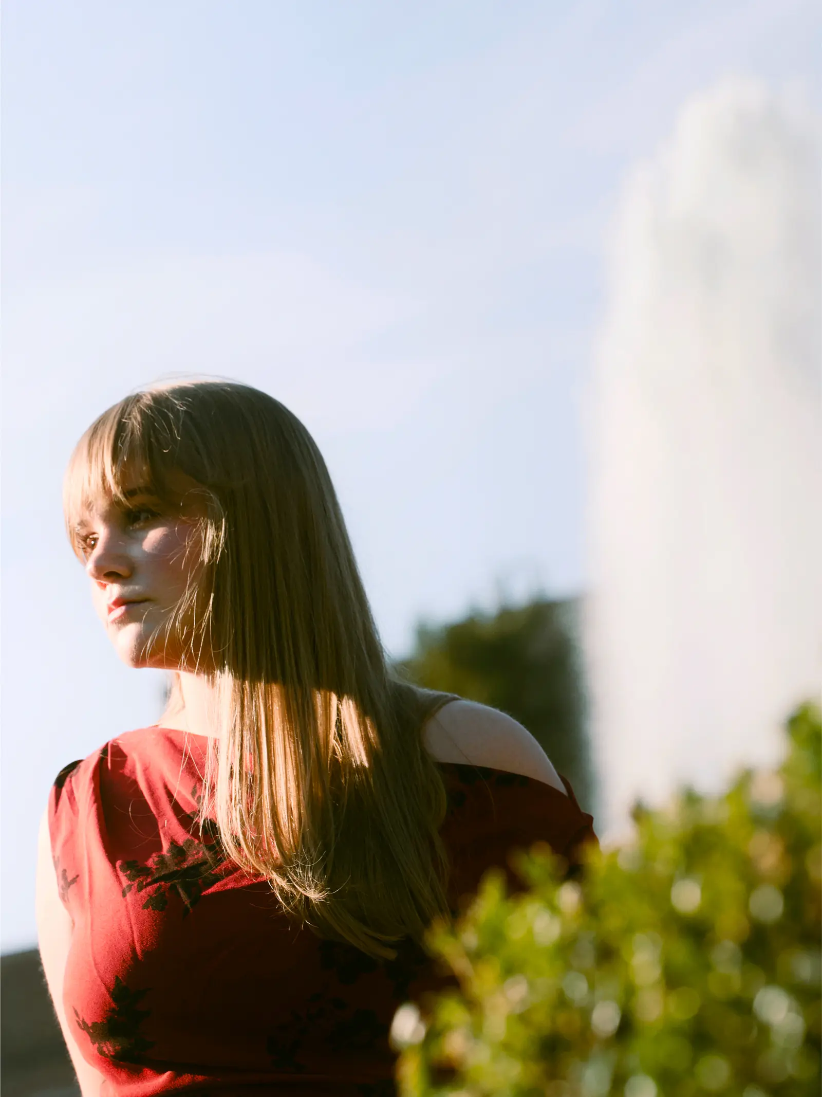 Senior in a red dress beside a sunlit garden hedge